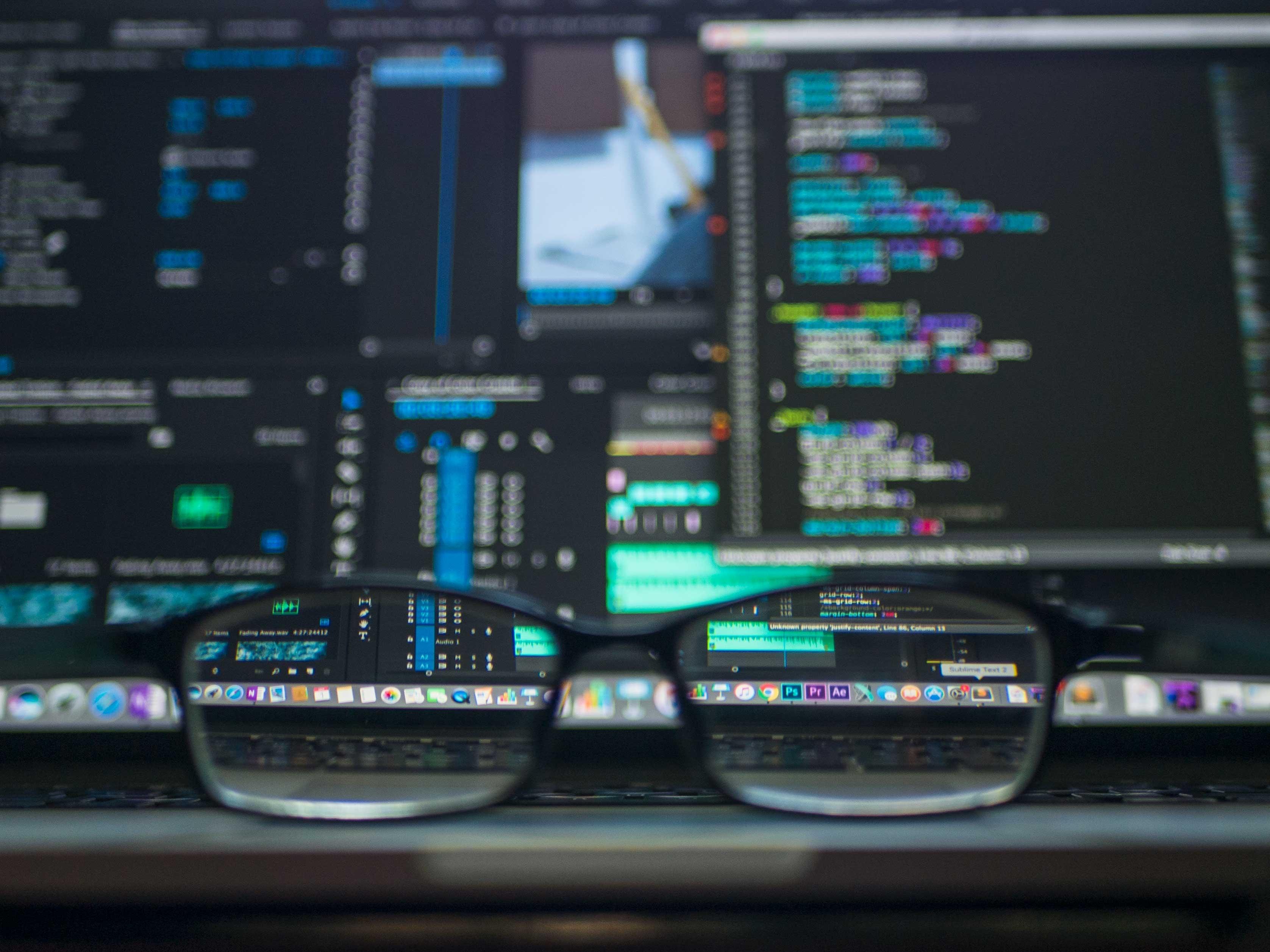 A photo of code on computer screens, blurred except a small part seen through glasses